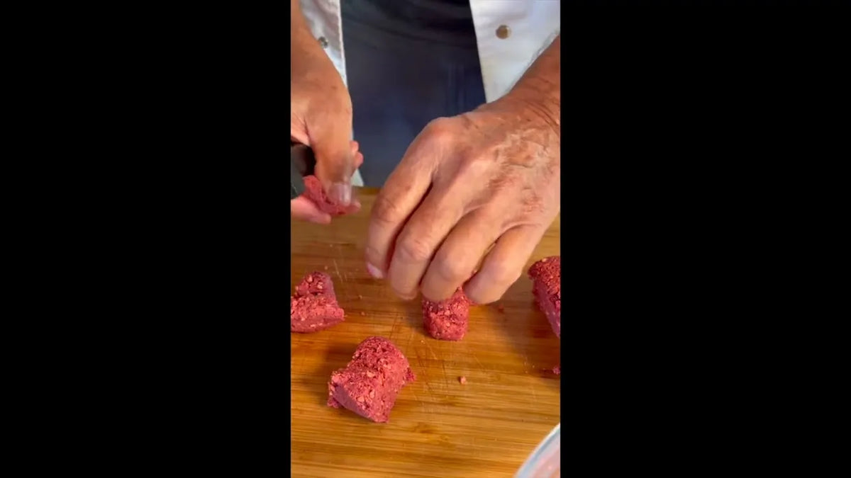 Hände schneiden rotes KIVEGAN Vleisch auf einem Holzbrett in Würfel